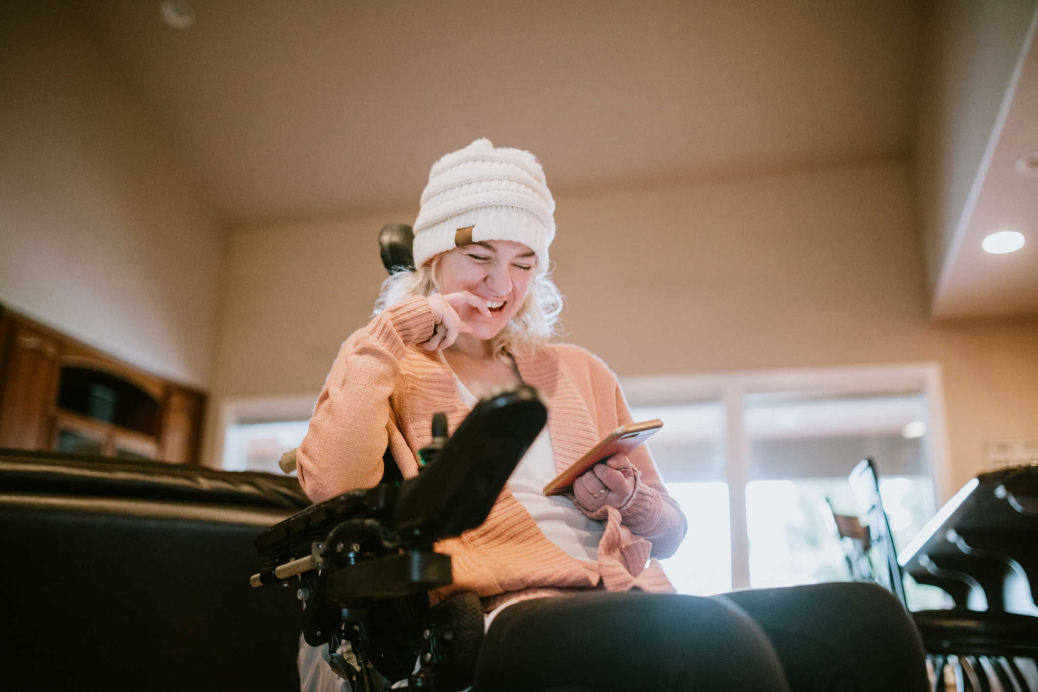 An independent young adult woman with cerebral palsy going about some of her daily routines at home. She smiles while browsing social media apps on her phone.