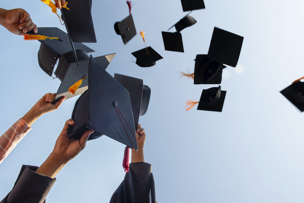 Cropped Hands Of People Throwing Mortarboards Against Clear Sky