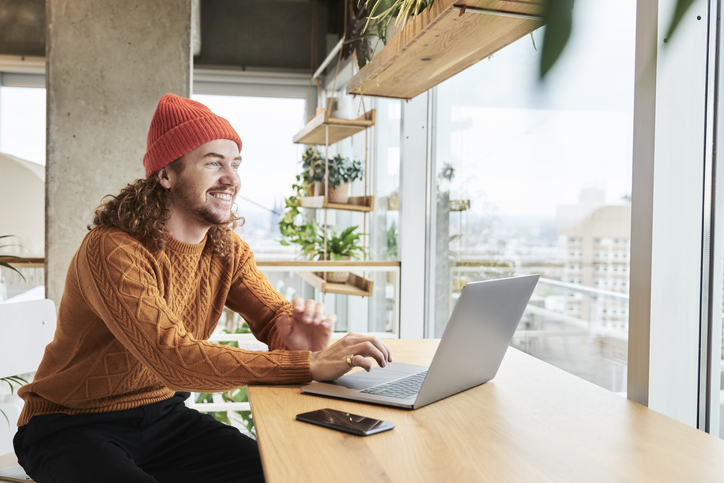 Smiling man wearing knit hat using laptop sitting at home