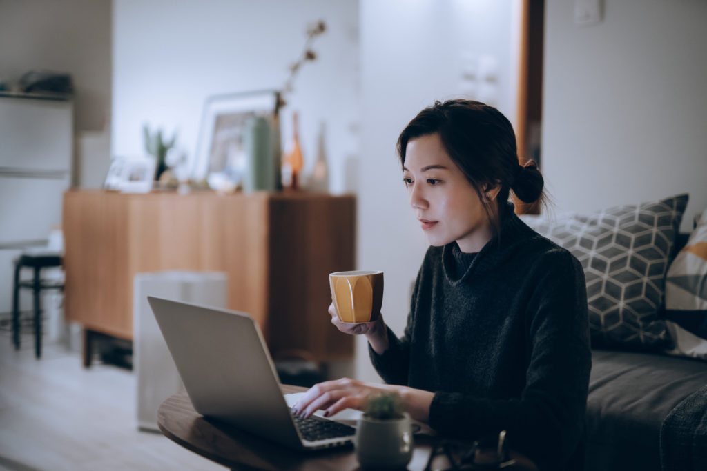 Busy concentrated young Asian woman working from home, working on laptop till late in the evening at home. Home office, overworked, deadline and lifestyle concept