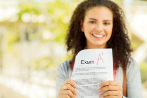 Portrait of successful female student showing exam result with A+ grade on university campus.