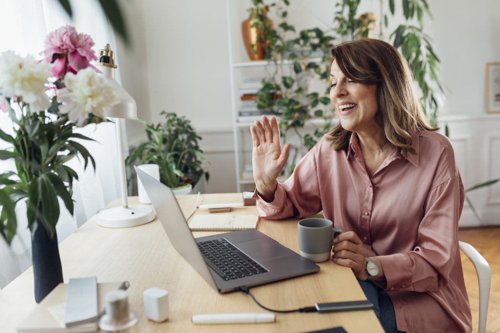 Smiling mature woman attending an online meeting from the comfort of her home office.