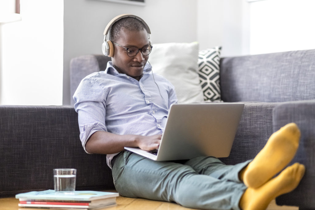Young man sitting on the floor in the living room using laptop and headphones