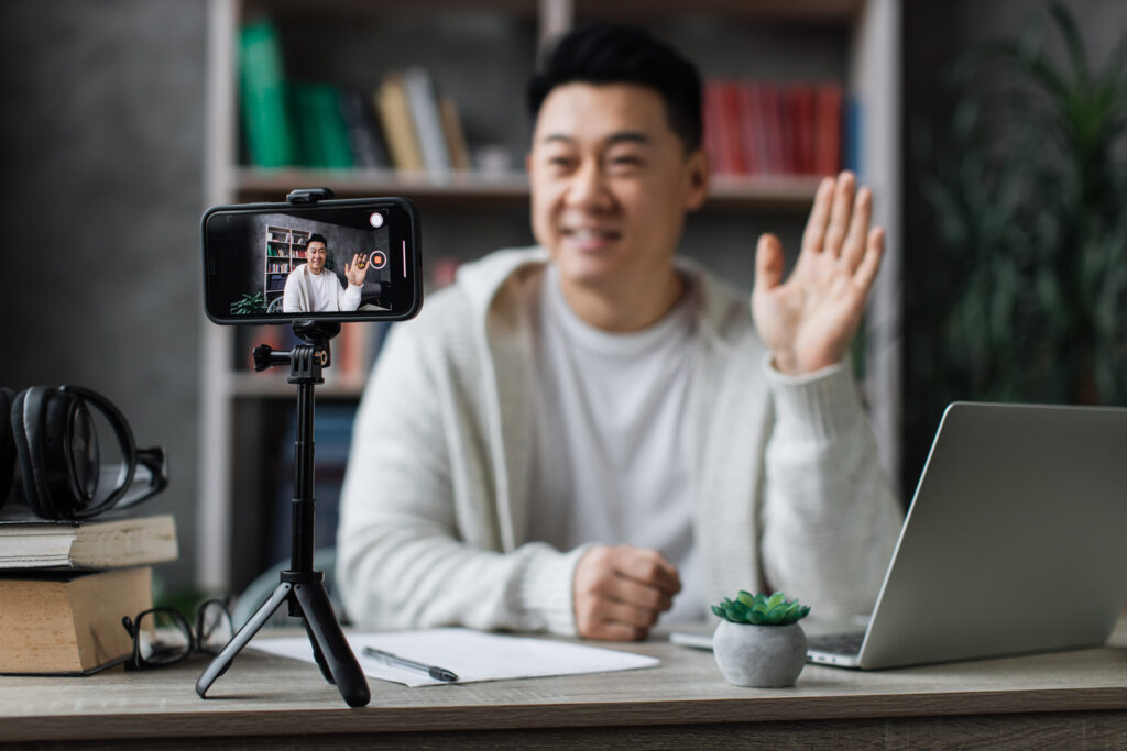 asian man in casual clothes talking and gesturing while recording video on modern phone