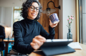 Smiling mature businesswoman sitting at cafe reading email on her digital tablet while having coffee. Female business professional using tablet computer and drinking coffee at coffee shop.