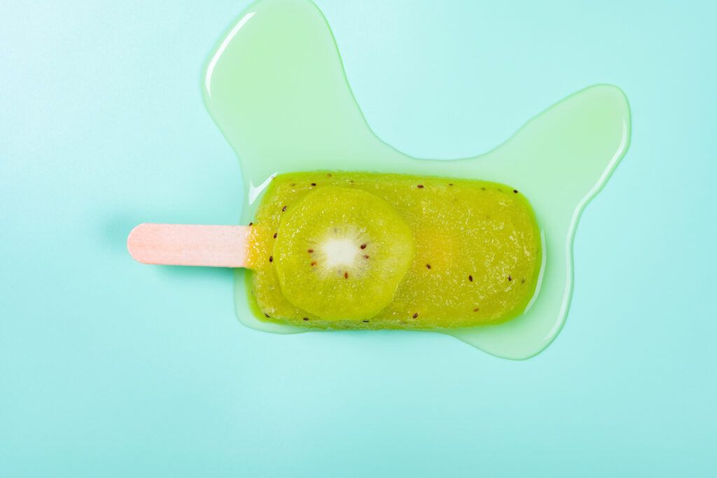 half melted watermelon and pineapple flavor popsicle with slice of kiwi fruit on a light green background
