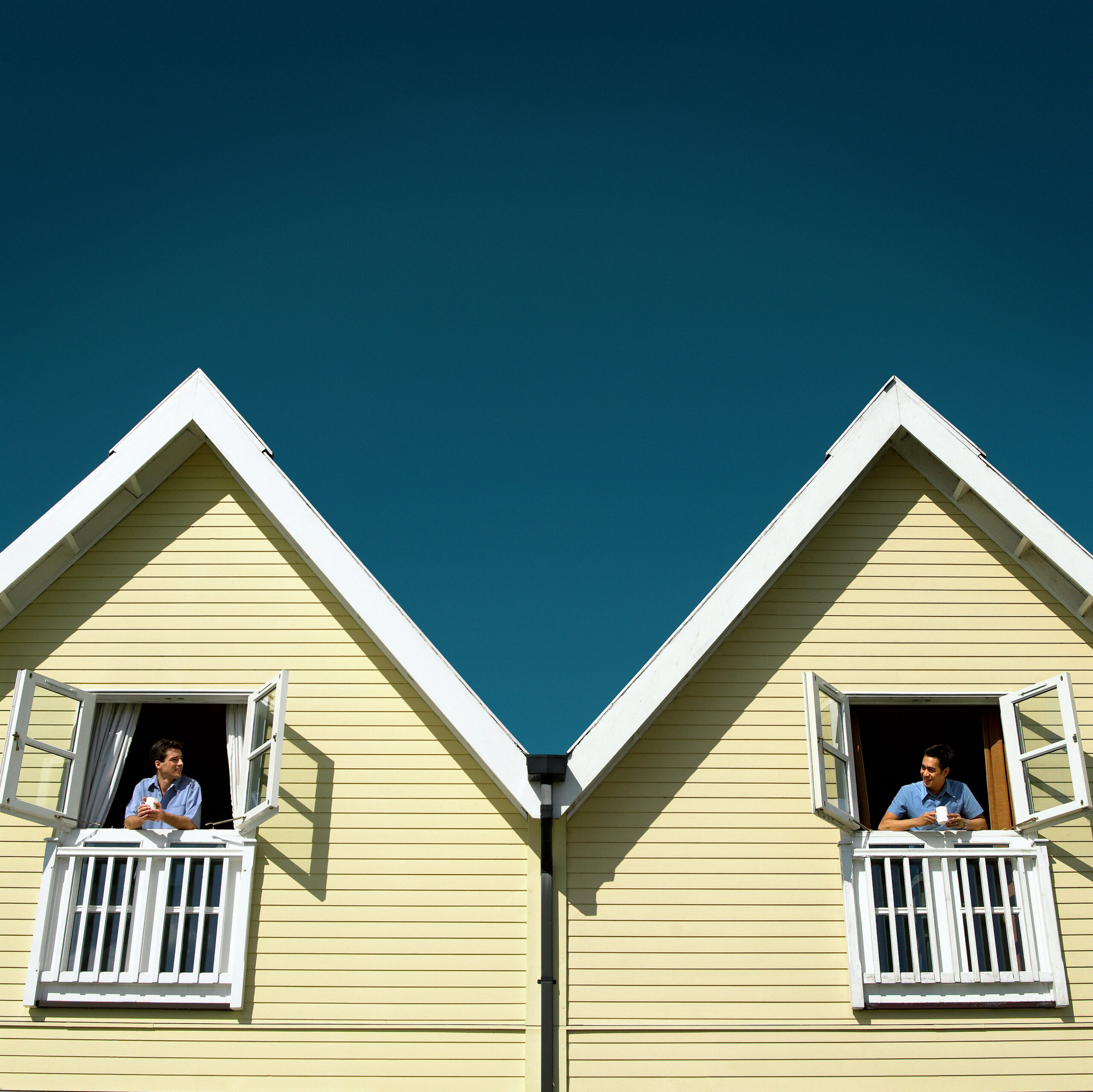 Two men leaning out of adjoining chalet windows (digital composite)
