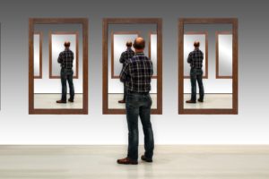 man looking at reflection in front of 3 mirrors on the wall