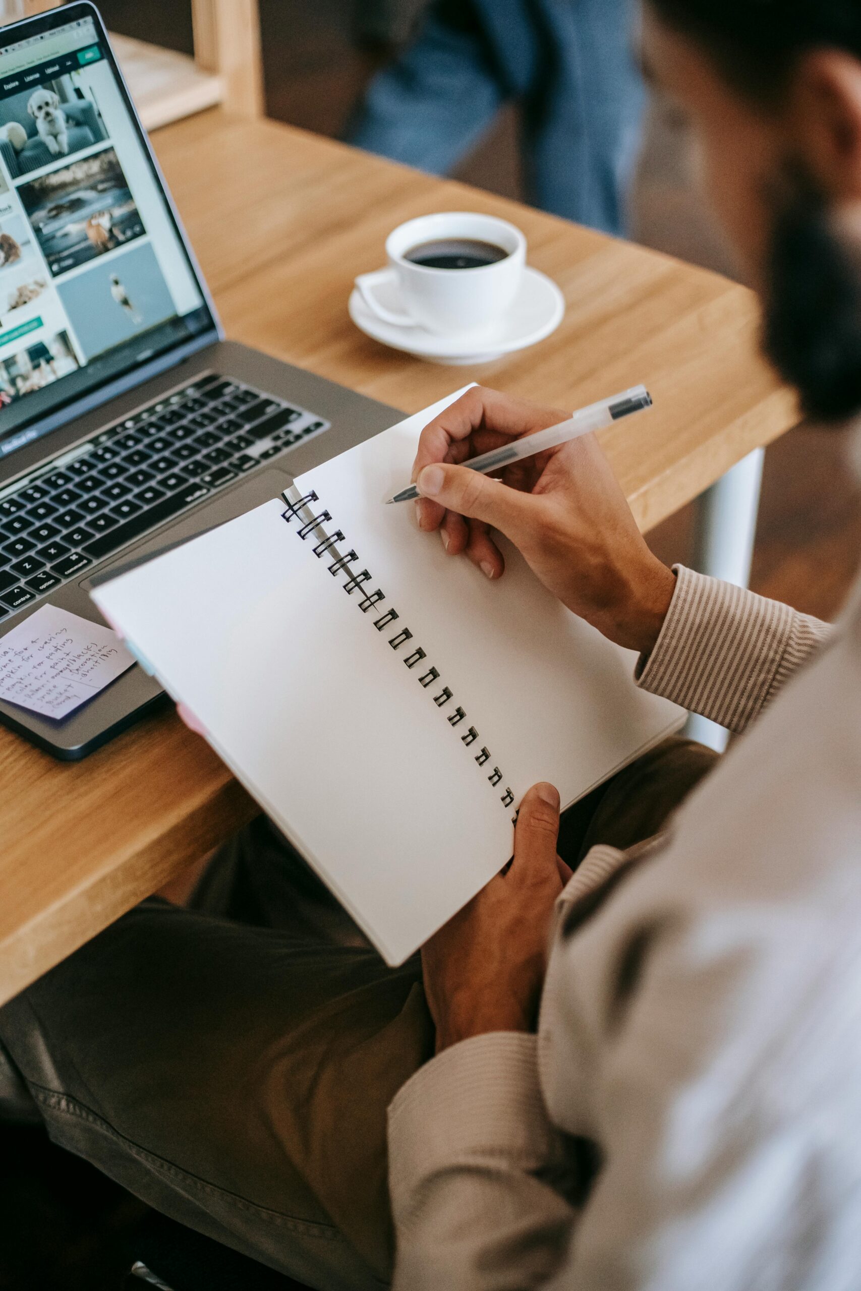 Man writing in notebook with laptop and coffee in home office setting.