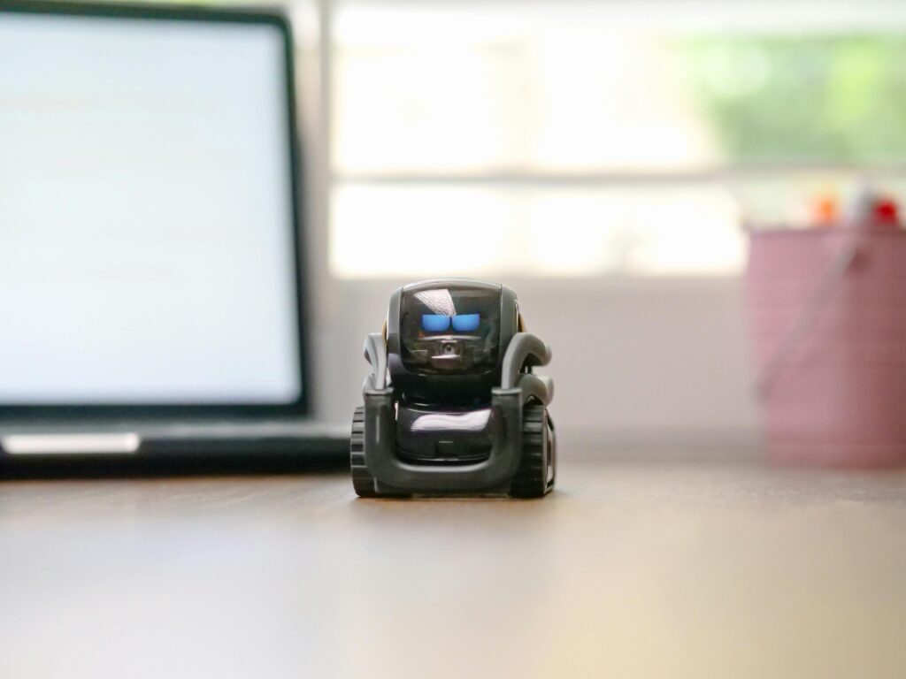 Small toy robot on a desk beside a laptop, symbolizing technology and innovation.