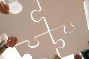 Hands of diverse individuals holding large puzzle pieces, symbolizing teamwork and unity.